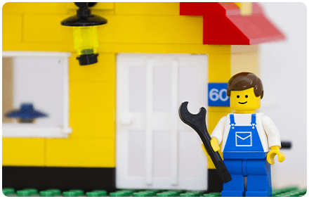 a lego house with a lego man in front of it holding a lego wrench.