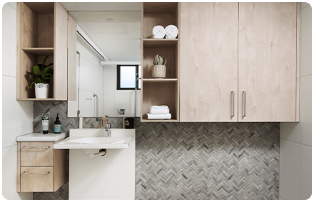 an image of an ndis bathroom renovation, with support handrails in the shower. there is a mirror above the sink and a wood cupboard next to it.