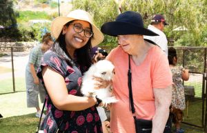 A photo of two women standing together on the lawn at Rocky Bay Mosman Park. Both ladies are wearing sun hats and the lady on the left is holding a fluffy white chicken and smiling at the camera. The Lady on the left is looking at the chicken.