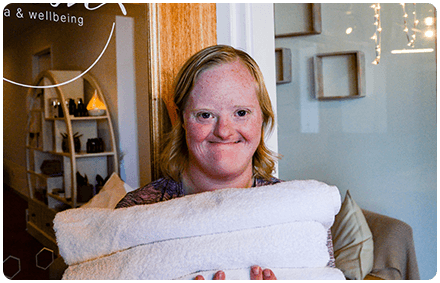 a person who lives with a disability is smiling and at work. she holds towels in her hands.