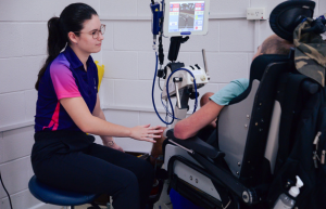 A female physio is assisting a customer with the functional electrical simulation bike