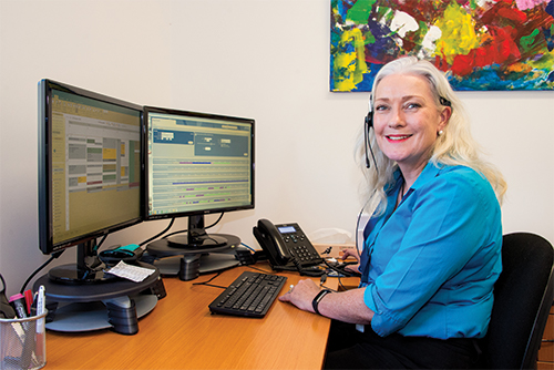 a disability support coordinator works at her desk and smiles at the camera.