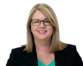 Woman in suit and glasses looks at camera smiling