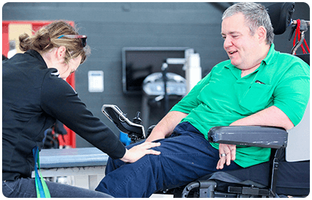 a rocky bay physiotherapist treats a client's knee. they are inside a physio gym. the client lives with a disability and sits in a wheelchair.