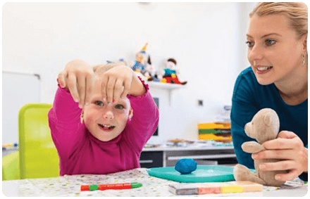 a rocky bay speech therapist and a child sit at an arts and craft table together. They smile and look at the child's hands.