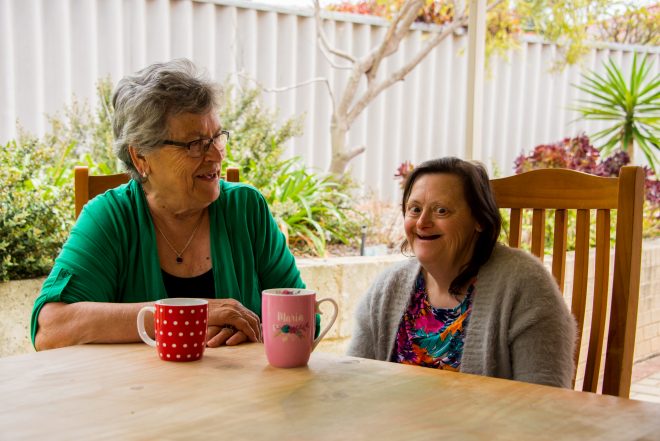 two elderly women sit together in specialist disability accommodation.