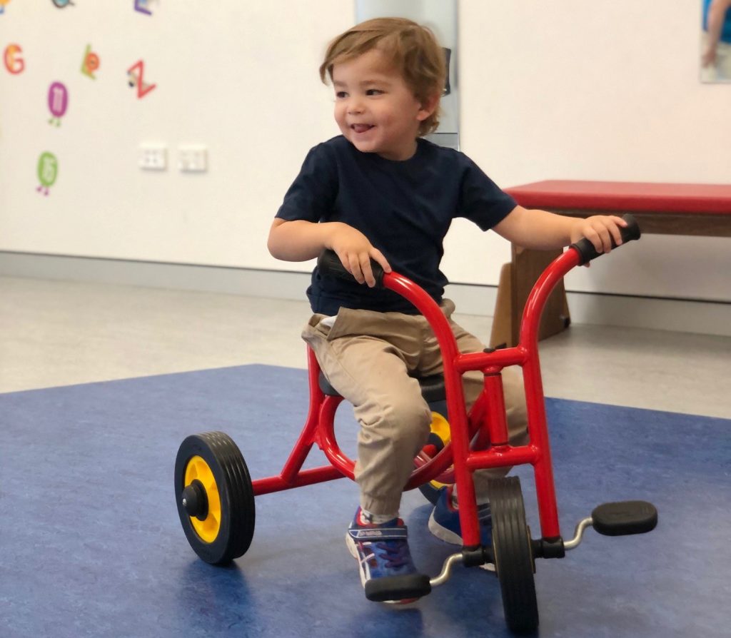 Emilio smiling and riding his new red tricycle