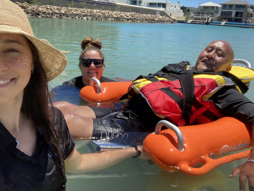 Moana using his beach wheelchair, accompanied by family and his Physio