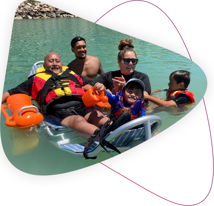 Customer Moana using his beech wheelchair in the water, surrounded by family