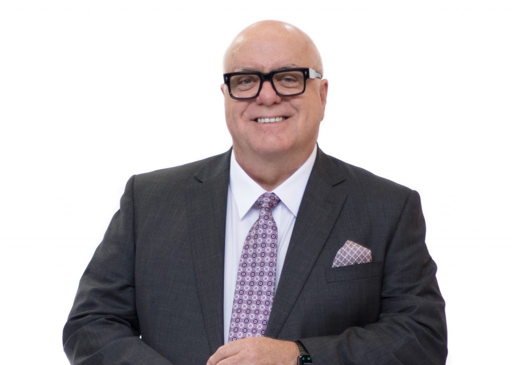 A head shot of incoming Chair Trent smiling, and in a dark suit and colourful tie