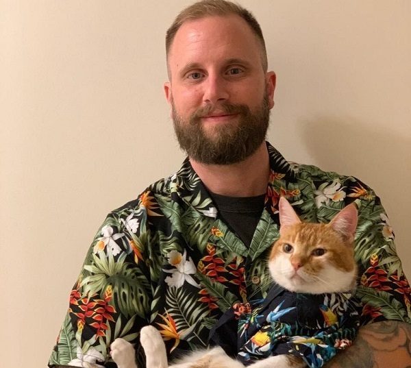 Howard holding his cat, both are wearing colourful Hawaiian shirts
