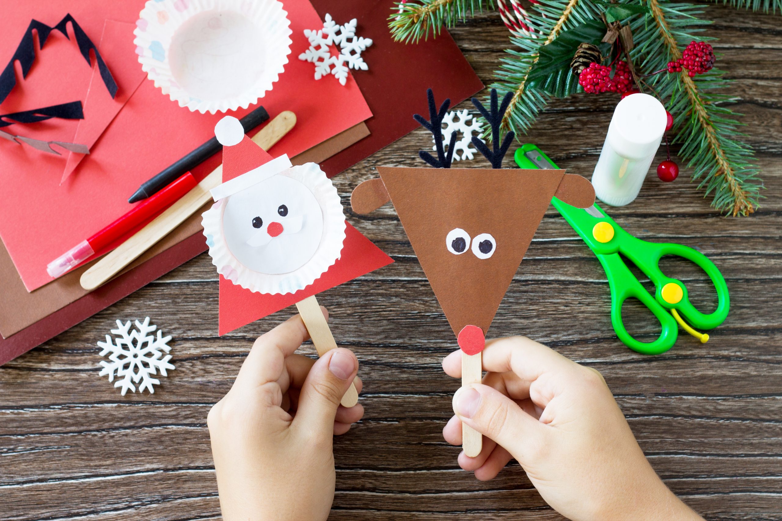 A child is holding Christmas Santa and Reindeer stick puppets