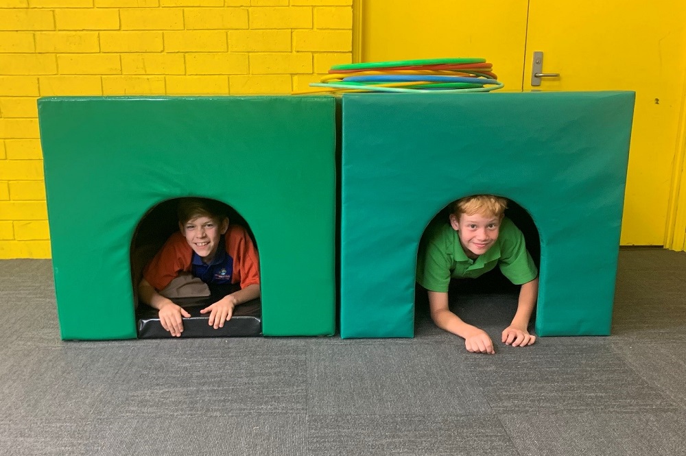 Two students are inside the green cosy cubbies. They are looking out for the cubby door and smiling at the camera.