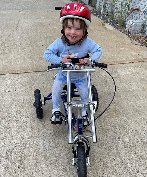 Evanee sits on her modified trike with a red helmet and is smiling