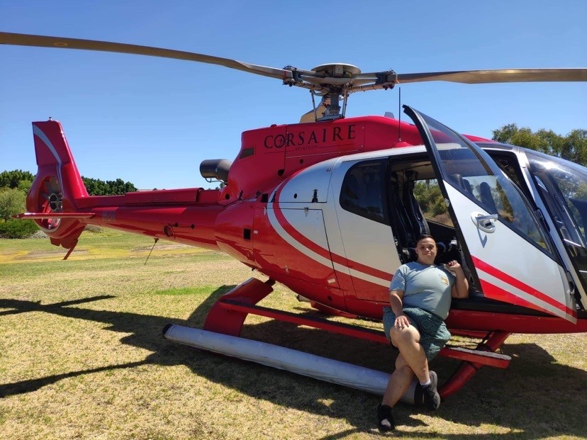 Fenton stands in front of a red helicopter whivh is perched on the grass near Crown Perth