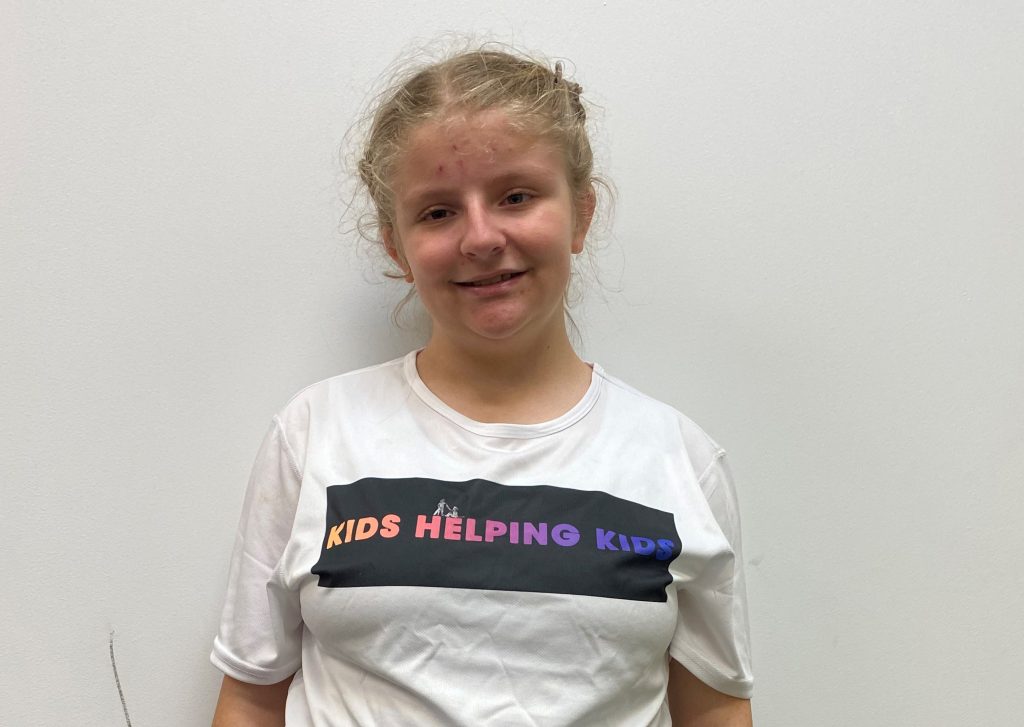 Young girl Angel in a white shirt with a 'Kids Helping Kids' logo