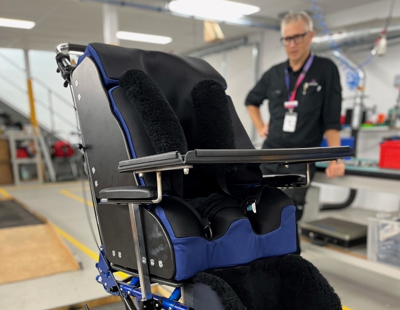 Equipment Manager Eamon stands behind a wheelchair fitted with the WheelAir cooling system