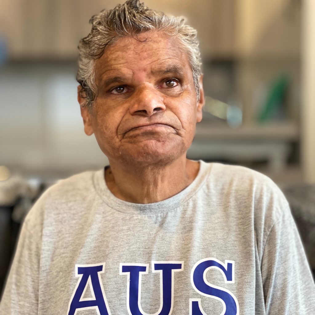 A portrait of Mark who is wearing a grey t-shirt with AUS written in blue across it. He is looking off camera