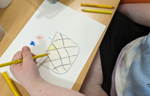 Photo of a young Rocky Bay customer participating in an art class at Lady Lawley Cottage in Cottesloe. She is drawing a picture of a basket with colourful flowers in it.