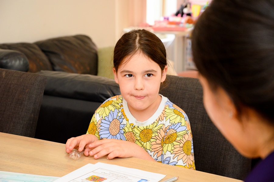 Harper with her therapist in her home. She is wearing a colourful top and sitting at a table.