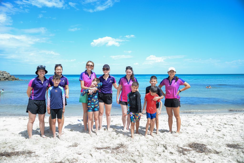 A group of Rocky Bay therapists with customers on the beach, the ocean is behind them.