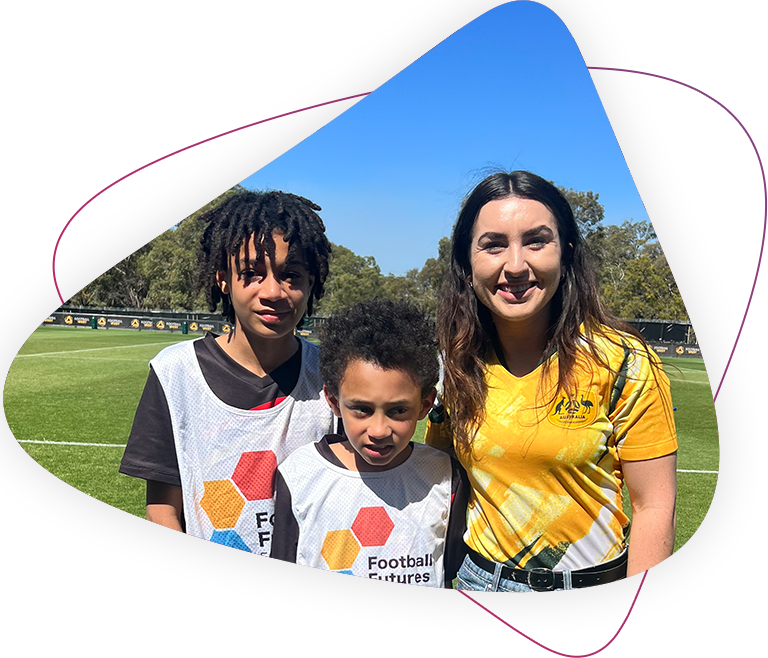 Matthew stands with his brother and Magenta on the Football field. They are wearing white football future shirts.