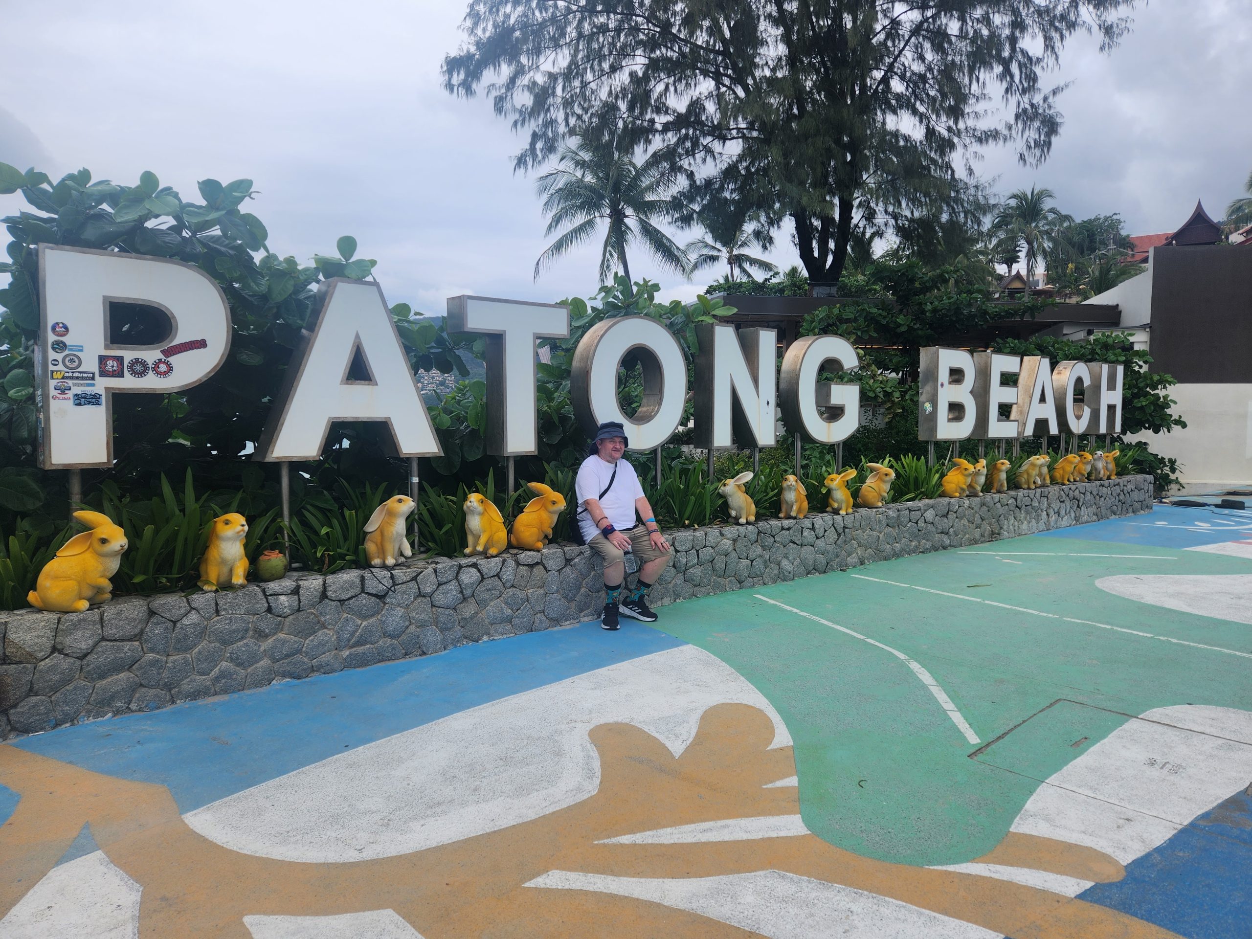 customer sits on a small wall with the writing "Patong beach' behind him