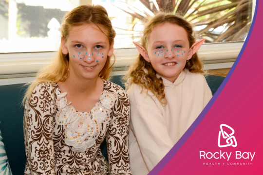 Two smiling children with face paint and elf ears sitting indoors.