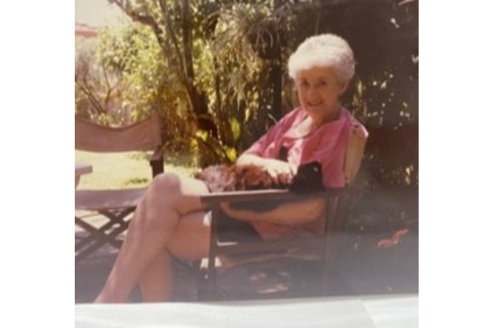 Image of Gloria Wilson, sitting on a chair smiling at the camera.