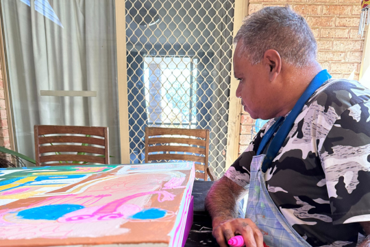 Customer sitting down and painting a canvas with bright colours.