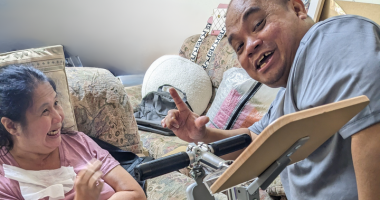 Customer Jasmine is sitting down using her SupaPedal device with husband beside her smiling