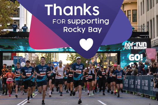 A group of people cross the finishing line of a HBF Run for a reason race, there is white text over the image that says' Thanks for supporting Rocky Bay.'