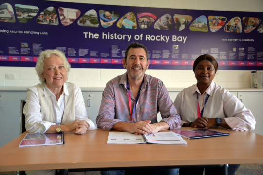 A photo of the Rocky Bay training team, from left to right sits Anne, Howard and Mariama. They are sat behind a table in a Rocky Bay training room.